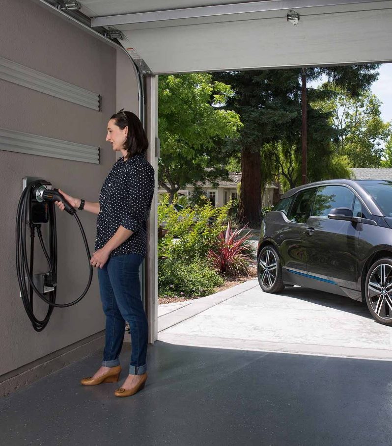 woman grabbing electric vehicle charger from garage wall