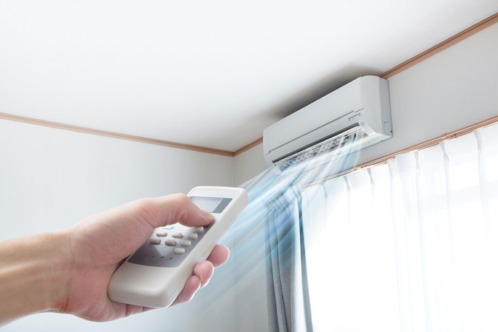 A person holding a remote control in front of a ductless air conditioner, adjusting the temperature settings.