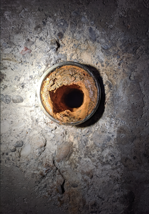 A galvanized pipe sticking out of a hole in a concrete wall.