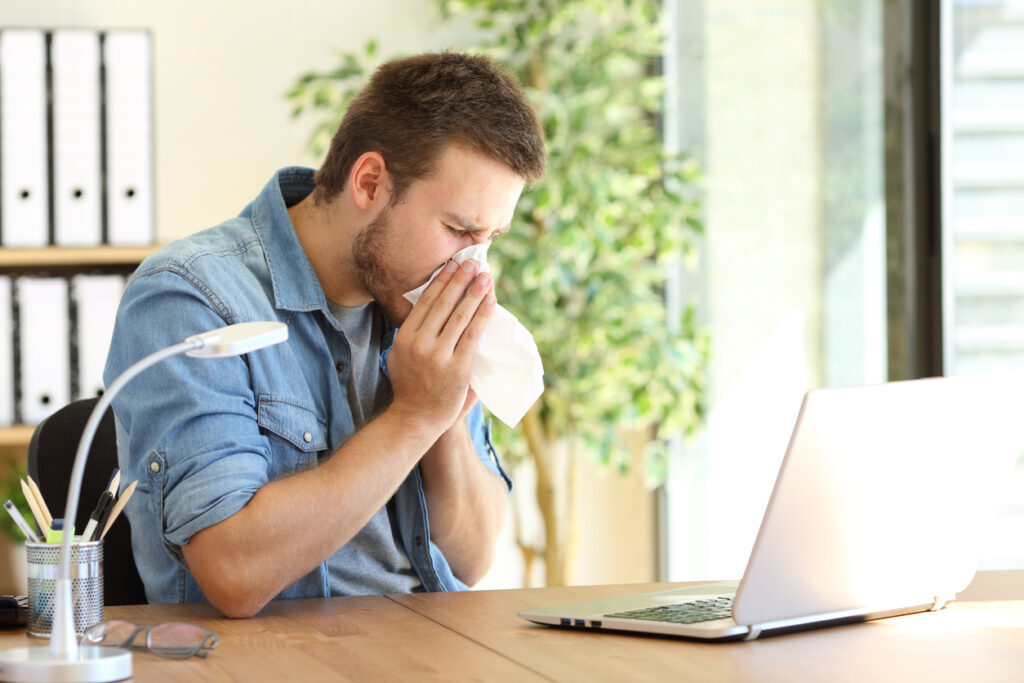Side view of man sneezing in to a tissue at his home office near a window